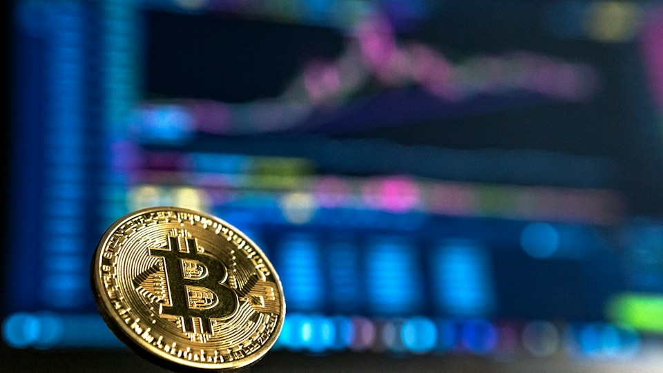 Physical Bitcoin coin in front of a trading screen